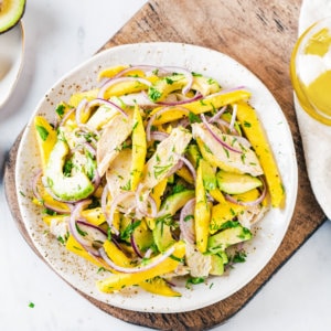 Avocado and chicken salad with mango on a white plate on a wooden board.