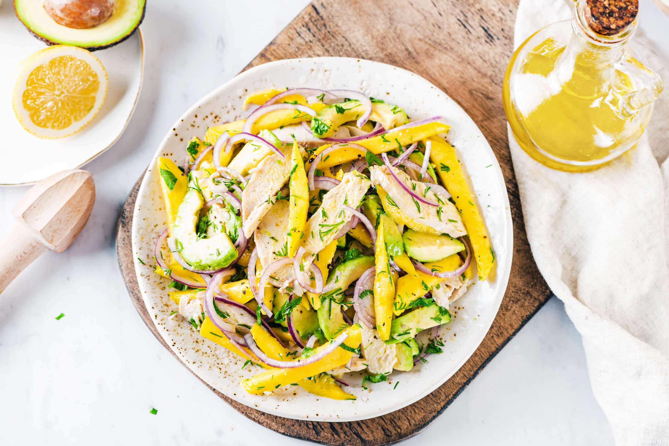 Avocado and chicken salad with mango on a white plate on a wooden board.