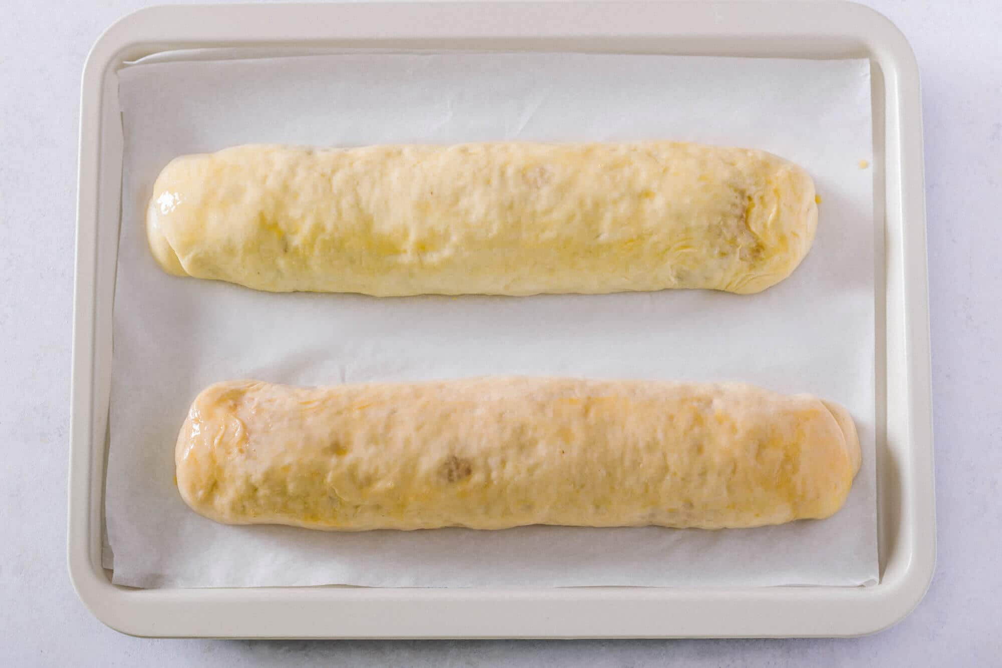 walnut-roll-rolled-up-with-egg-wash-on-parchment-paper-and-a-baking-tray