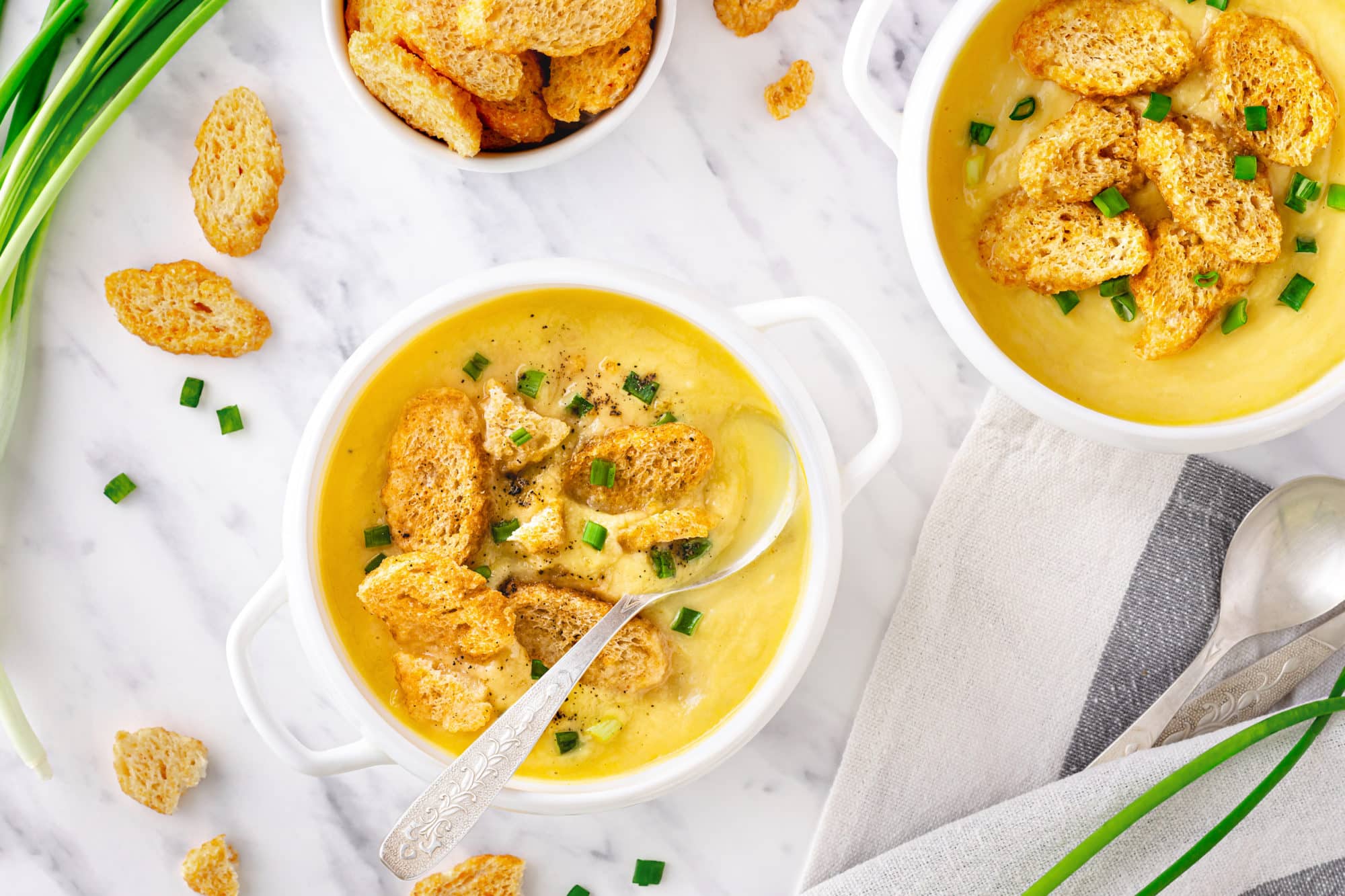 a white bowl of creamy cauliflower soup with croutons and a spoon.