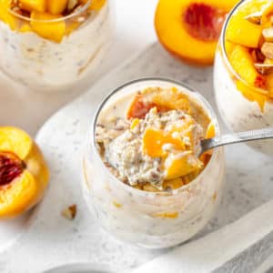 peach-overnight-oats-on-a-marble-board-with-a-spoon-and-with-cinnamon-and-peaches-in-the-background