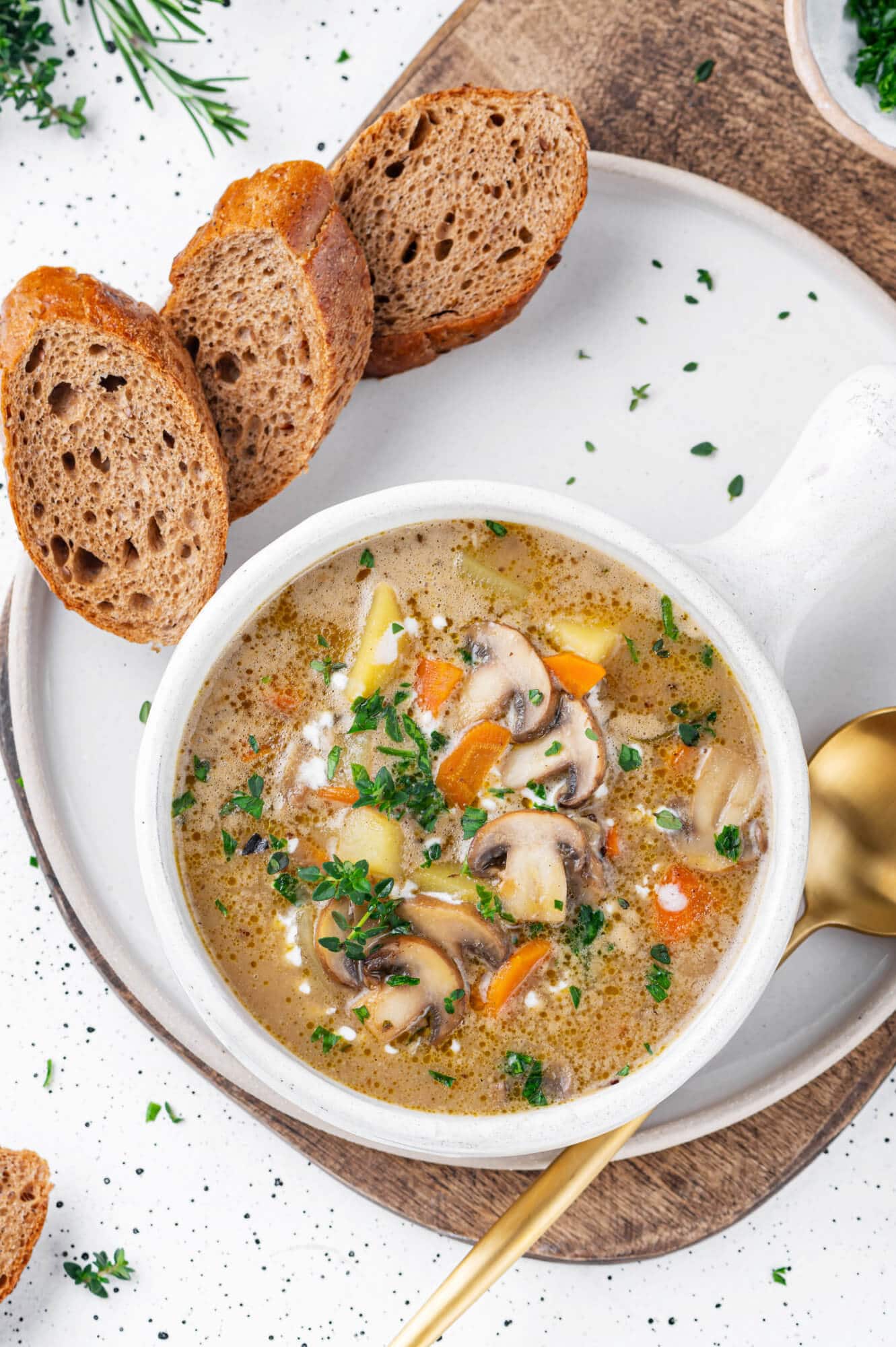 A white bowl of mushroom soup on a plate with a spoon, parsley for garnish, and toast for serving.