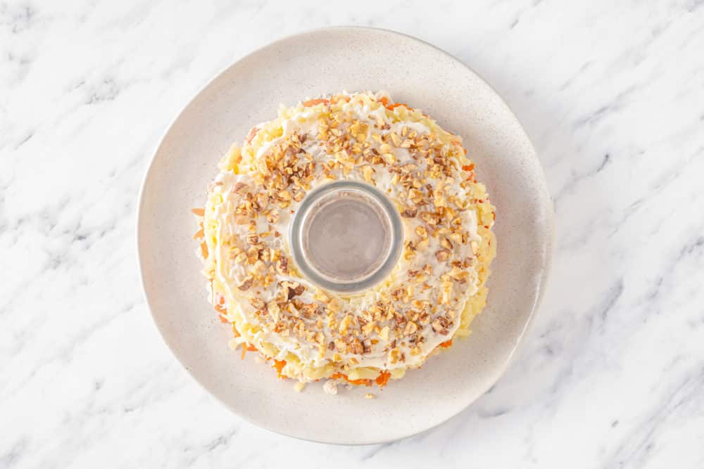 walnuts atop mayonnaise and a grated potato salad layer on a white plate with a glass cup in the center.