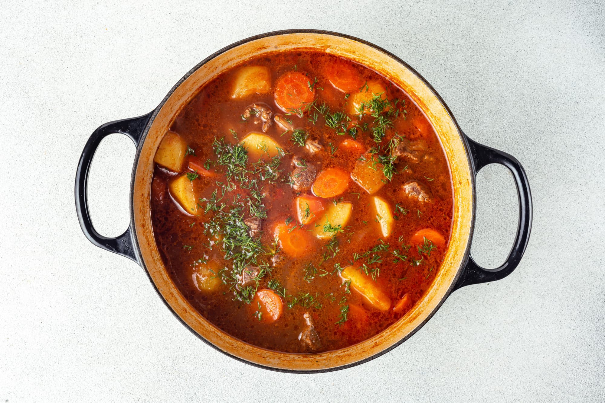 one pot meat stew cooking in a large black pot with dill sprinkled on top.