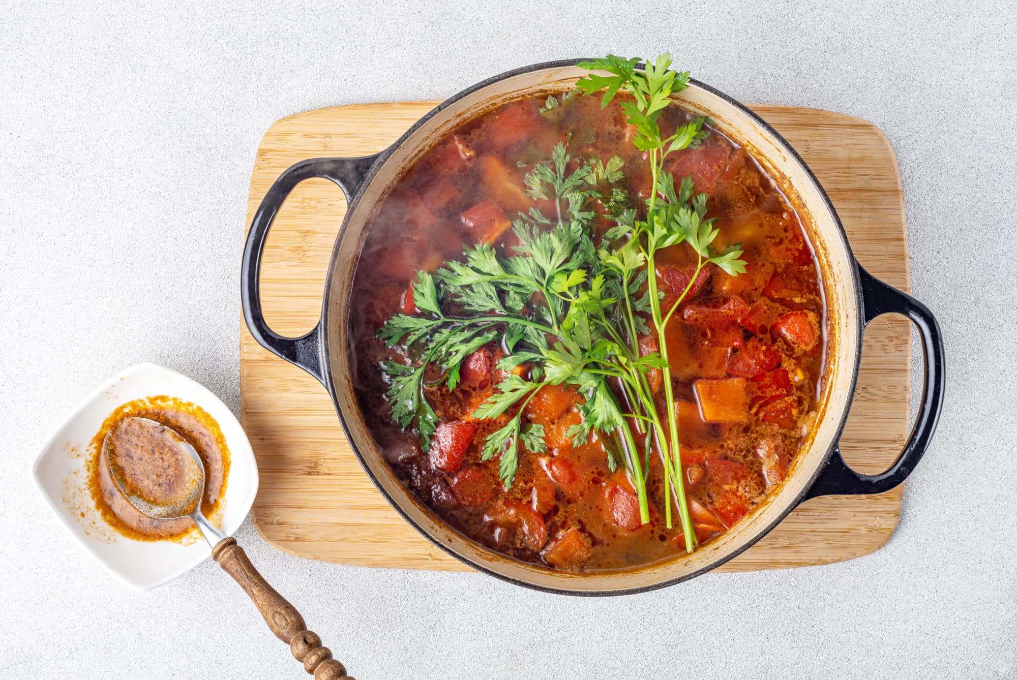 Soup in a pot with long sprigs of parsley on top and a white bowl with a spoon on the side.