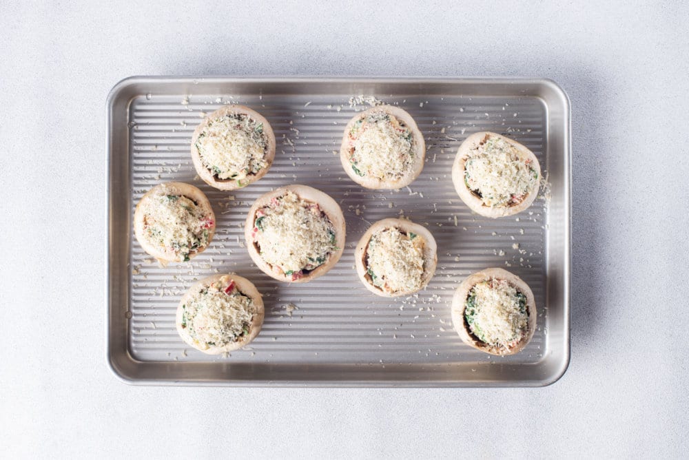 a baking tray with stuffed mushroom bites waiting to be baked with cheese sprinkled on top.