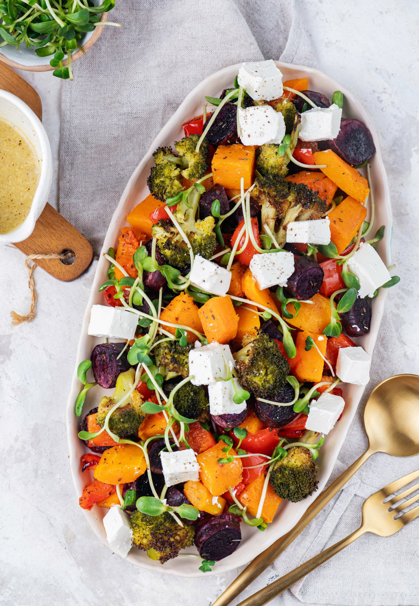 roasted vegetables in a large dish with dressing in a bowl on the side.