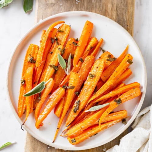 Chopped and roasted carrots on a white plate with sage.