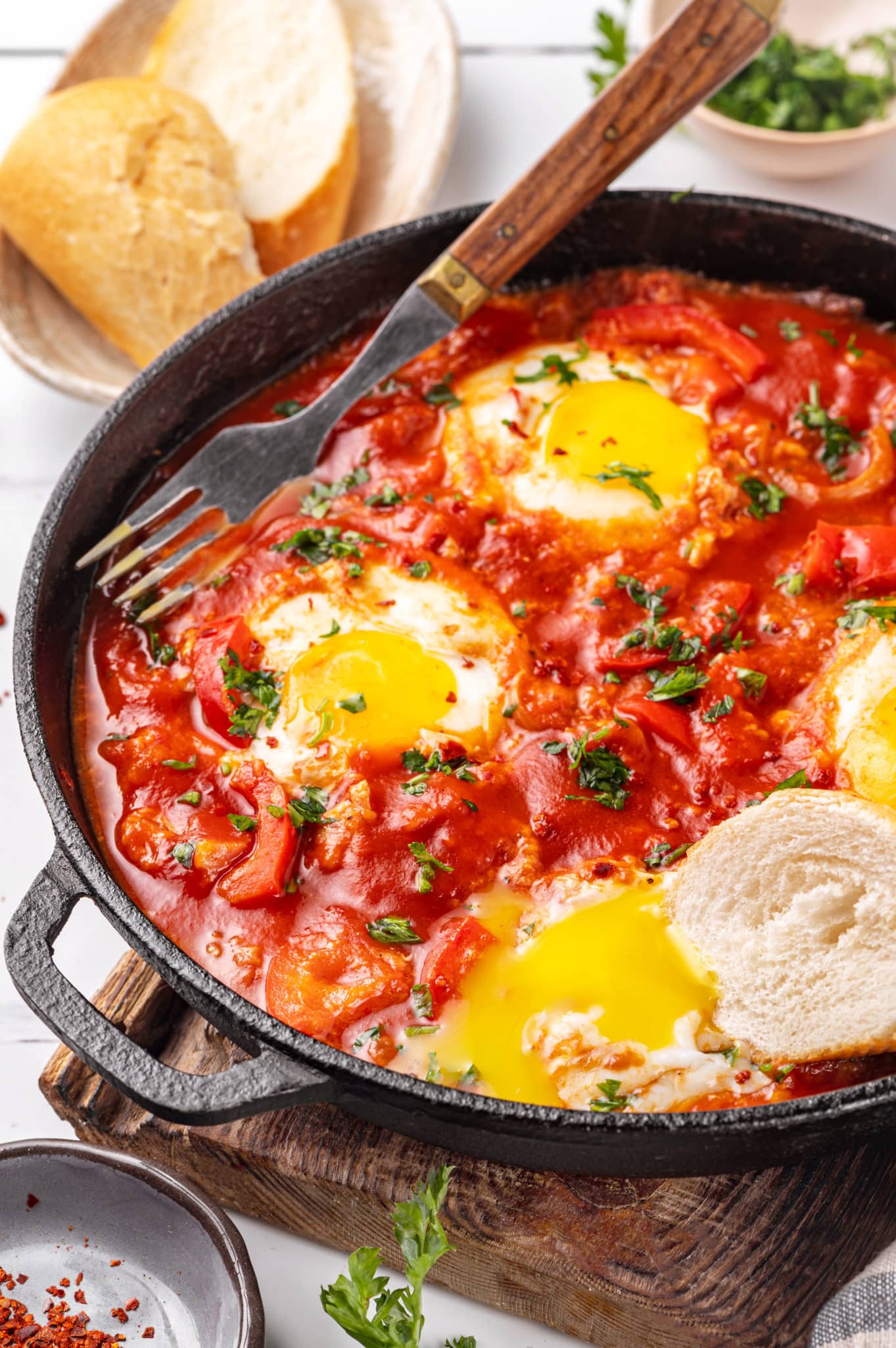 a piece of bread in a skillet of shakshuka with a fork.