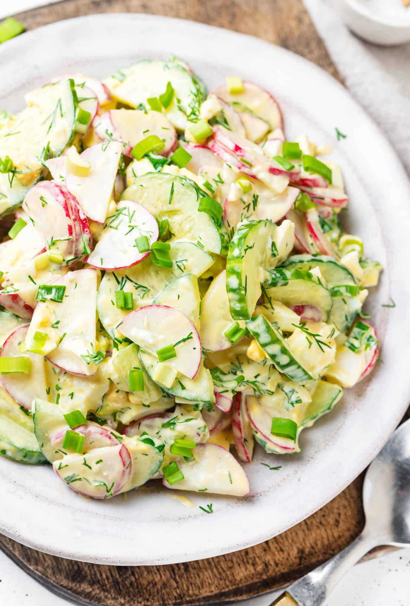 Radish cucumber salad with green onion and dill on a white plate.