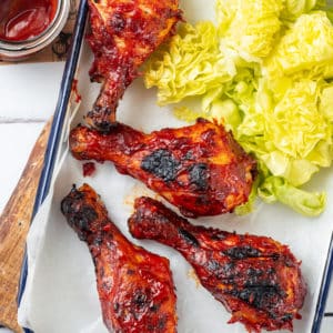 Grilled chicken drumsticks in a tray with lettuce on the side.