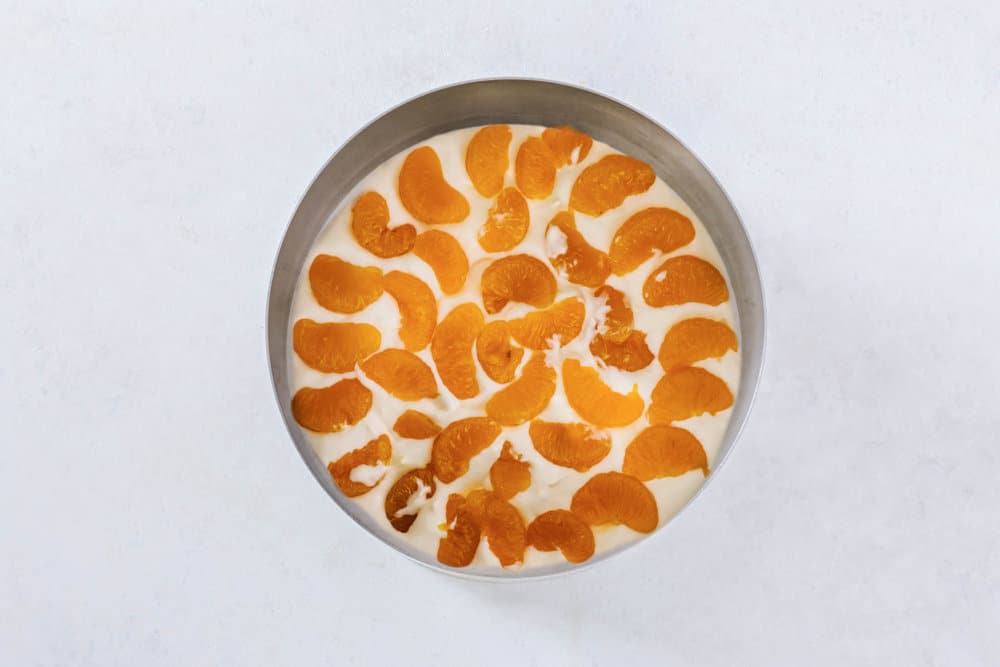 Mousse with mandarin pieces in it in a springform pan.