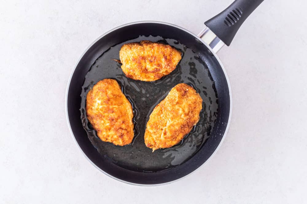 a black skillet with oil and sauteing chicken on it.