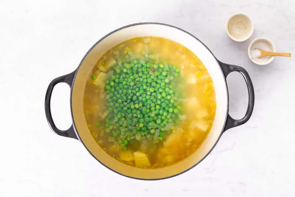 a white pot cooking soup with peas added on top.