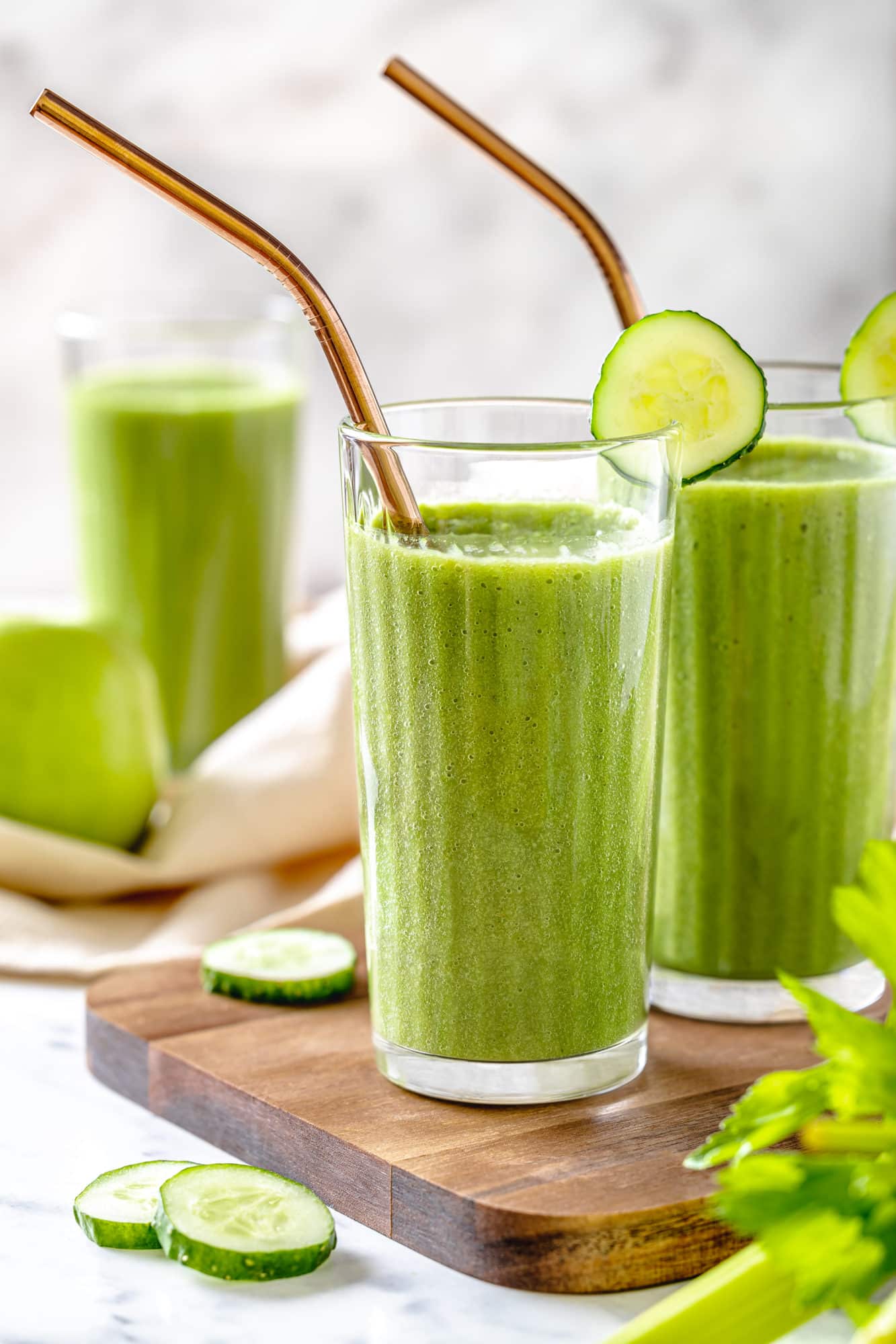 green smoothie in glasses with straws and cucumber slices.