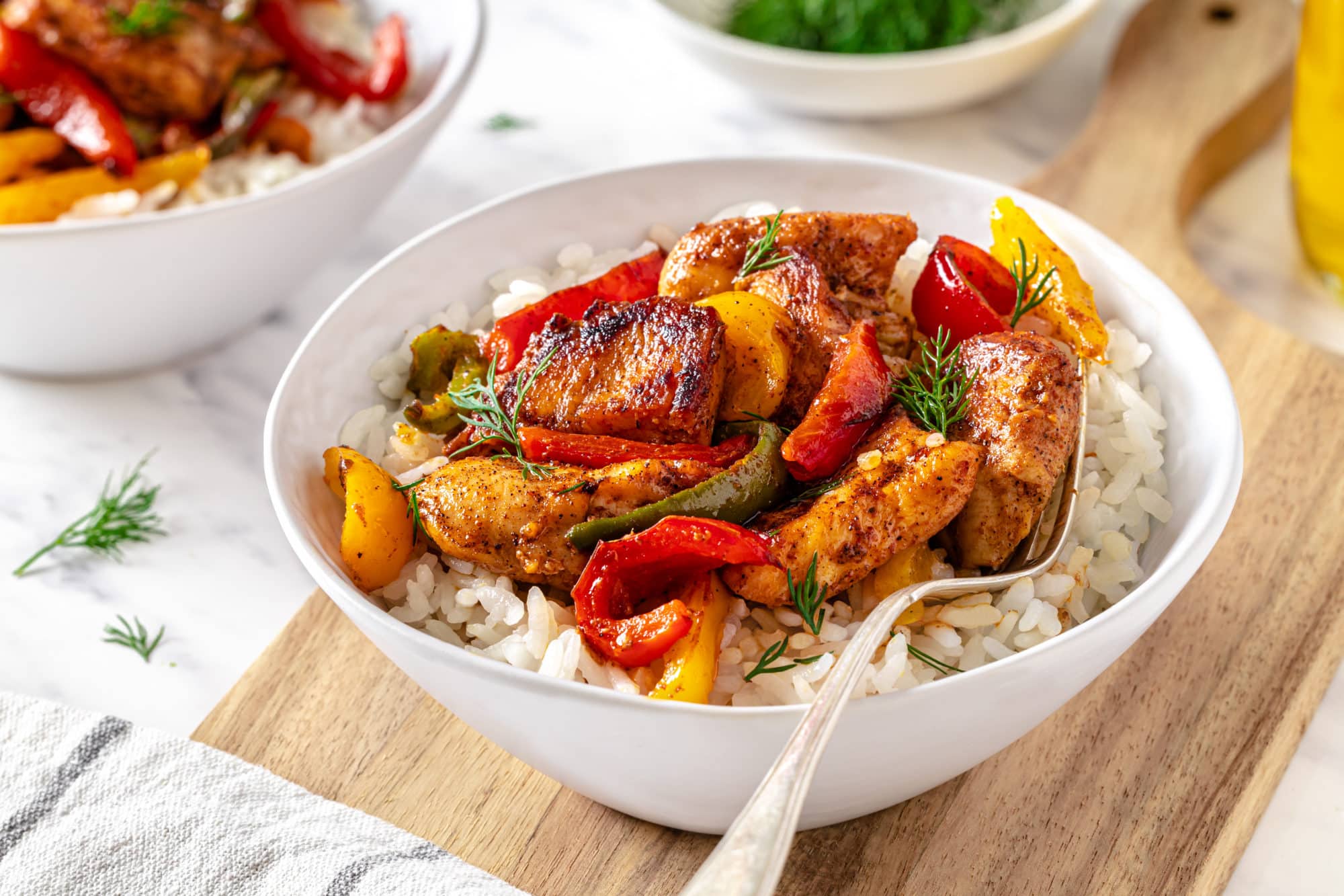 chicken-and-bell-peppers-with-rice-in-a-white-bowl-with-a-fork-on-a-wooden-board