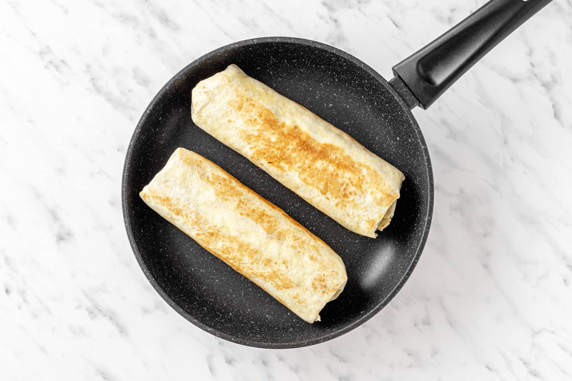 two burritos toasting in a black pan.