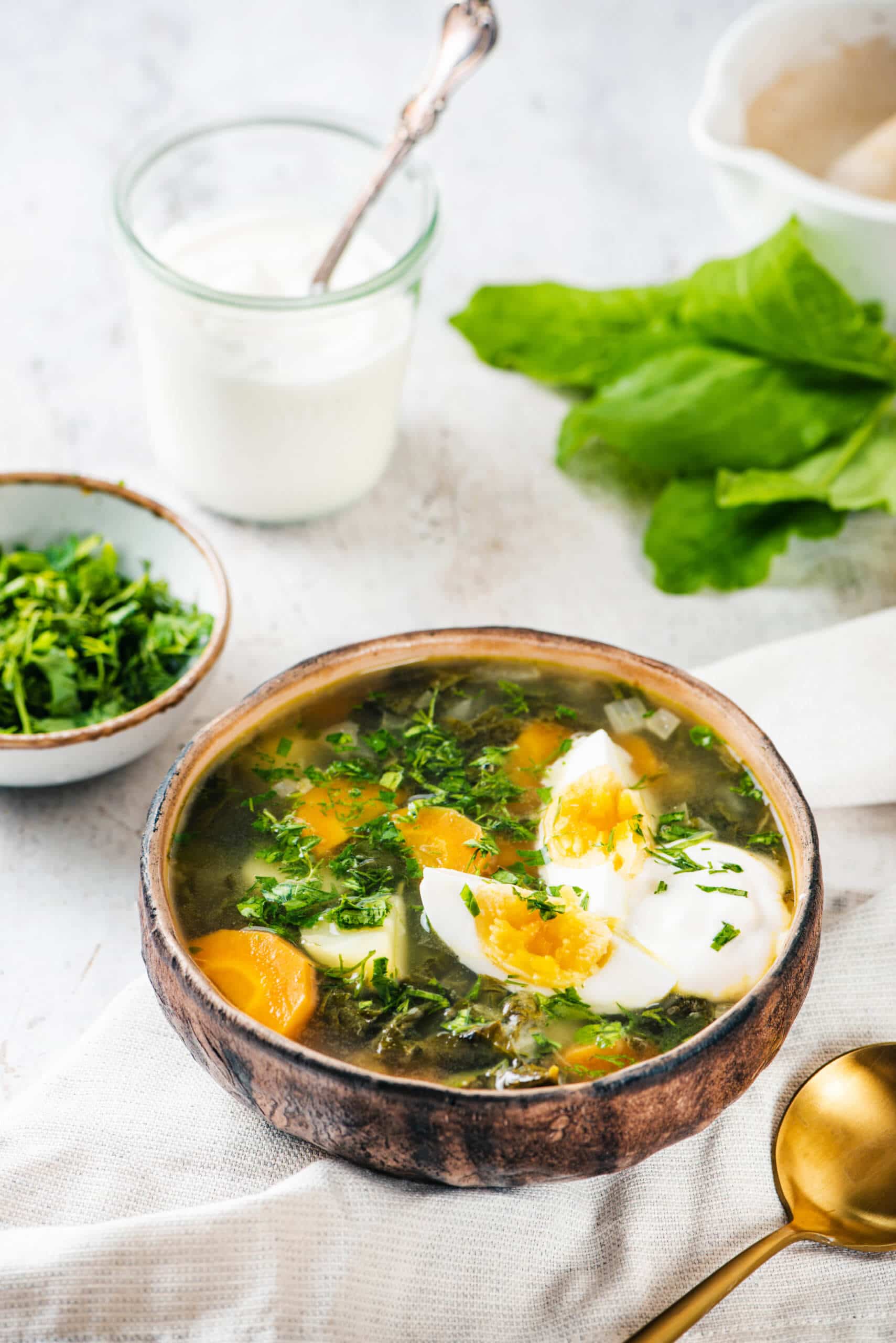 Sorrel soup in a brown bowl on a white towel with a gold spoon.