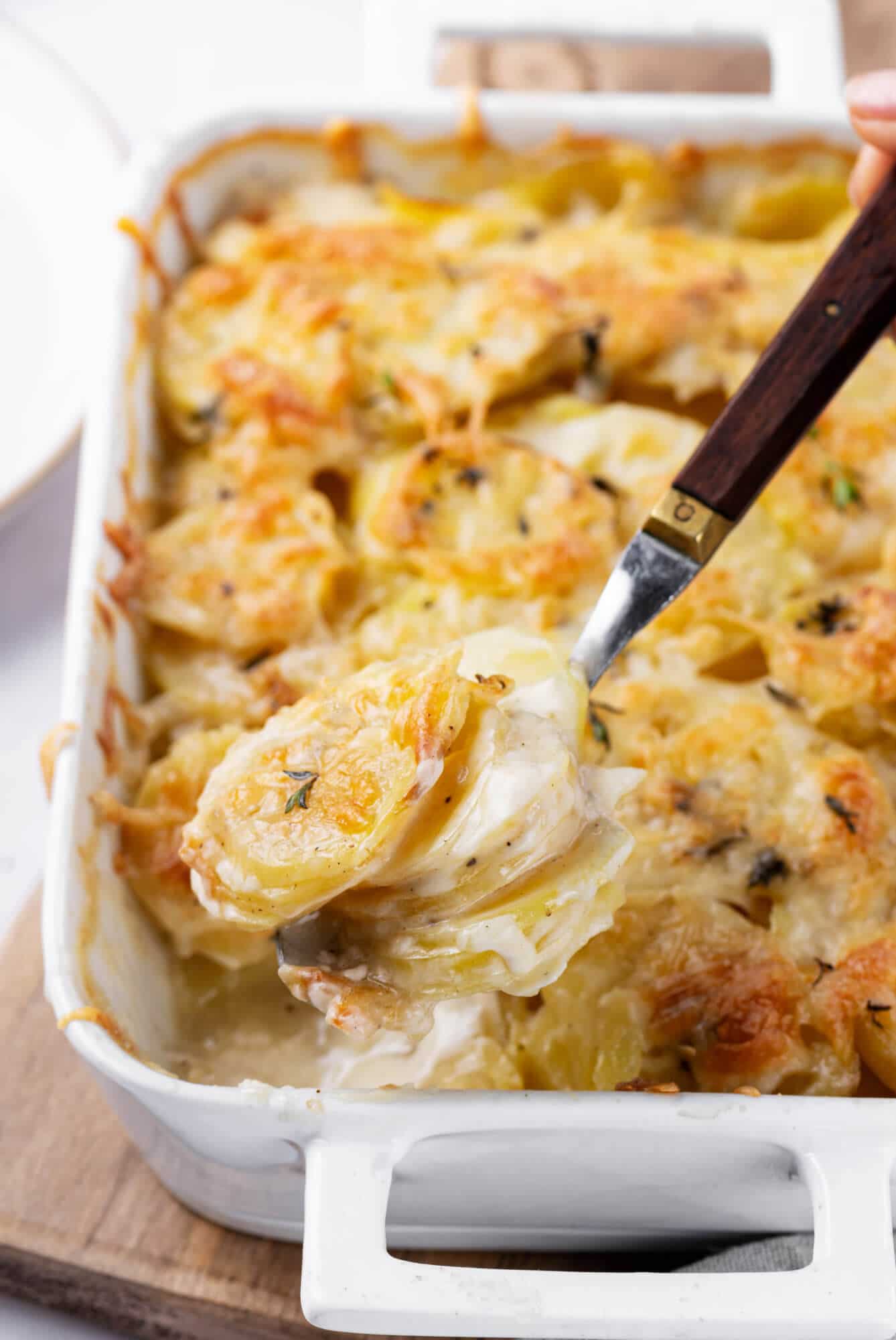 scalloped-potatoes-in-baking-dish-on-wooden-board-with-spoon