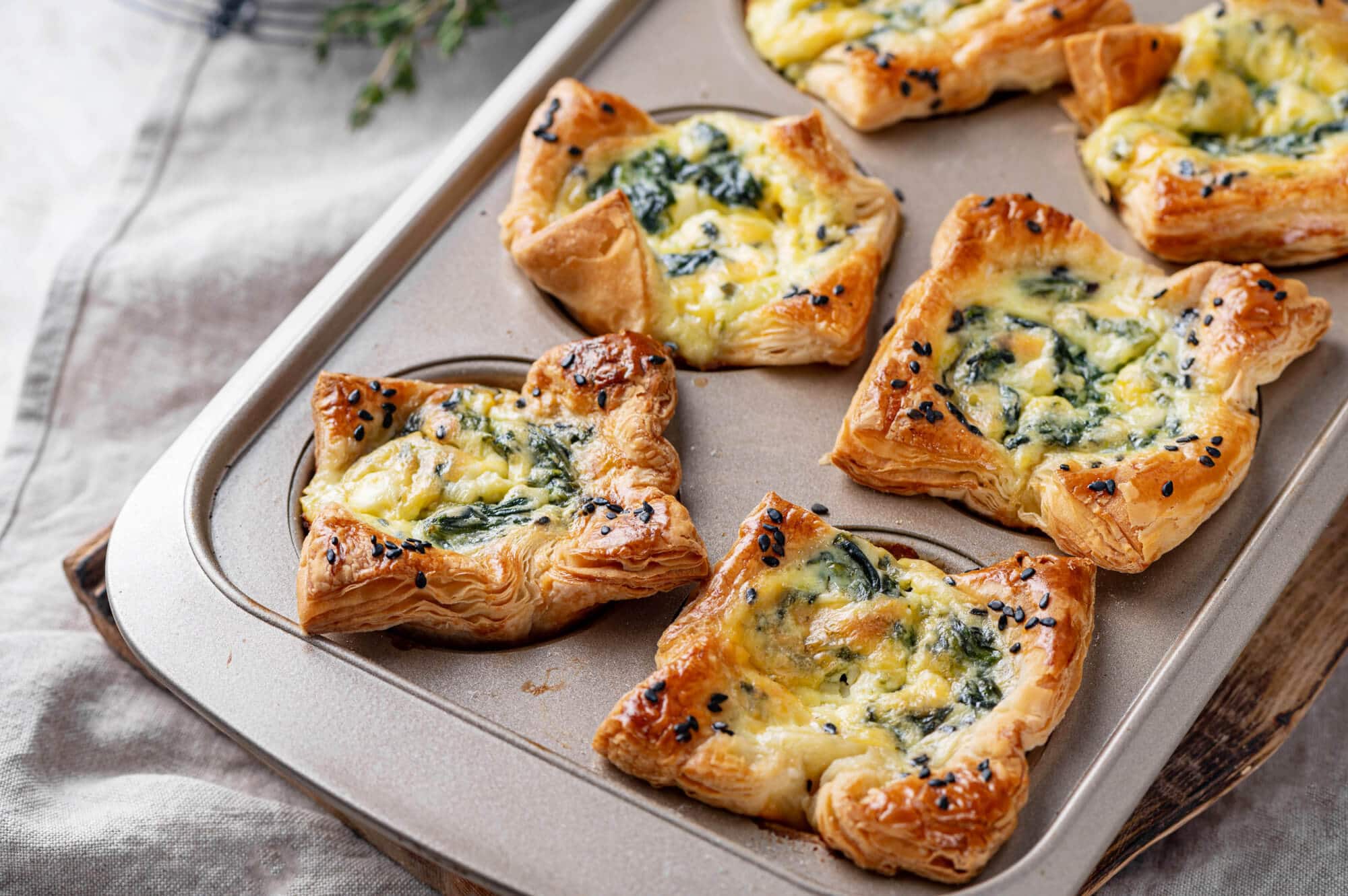 Spinach puffs in a muffin tin on a wooden board. 