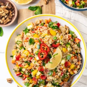 a yellow salad bowl filled with a quinoa salad on a wooden board and a white striped towel.