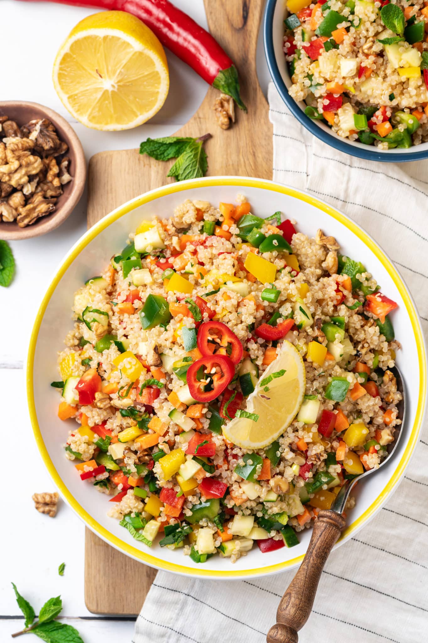 a yellow salad bowl filled with a quinoa salad on a wooden board and a white striped towel.