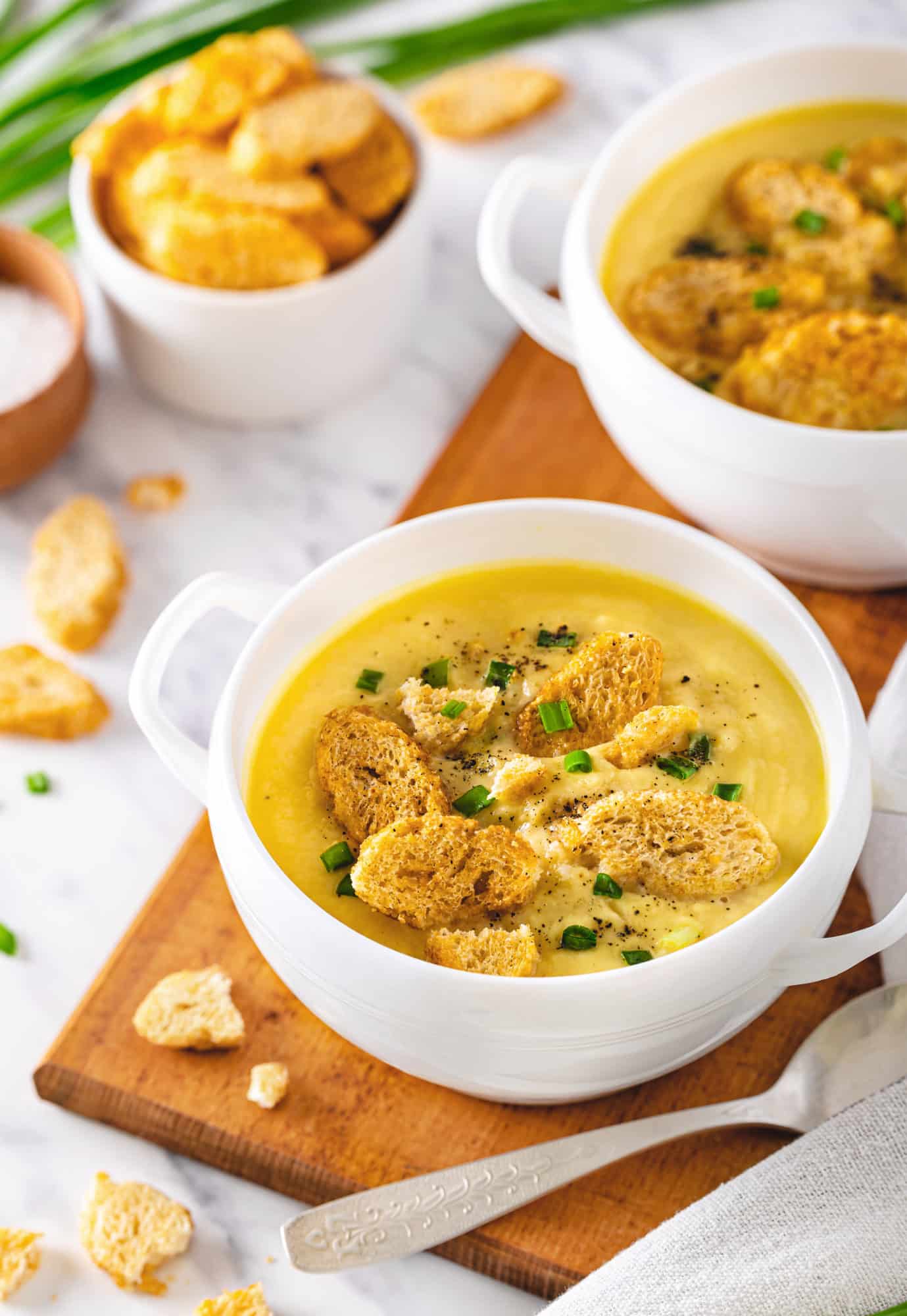 Cauliflower soup in two bowls on a wooden board with a spoon on the side.