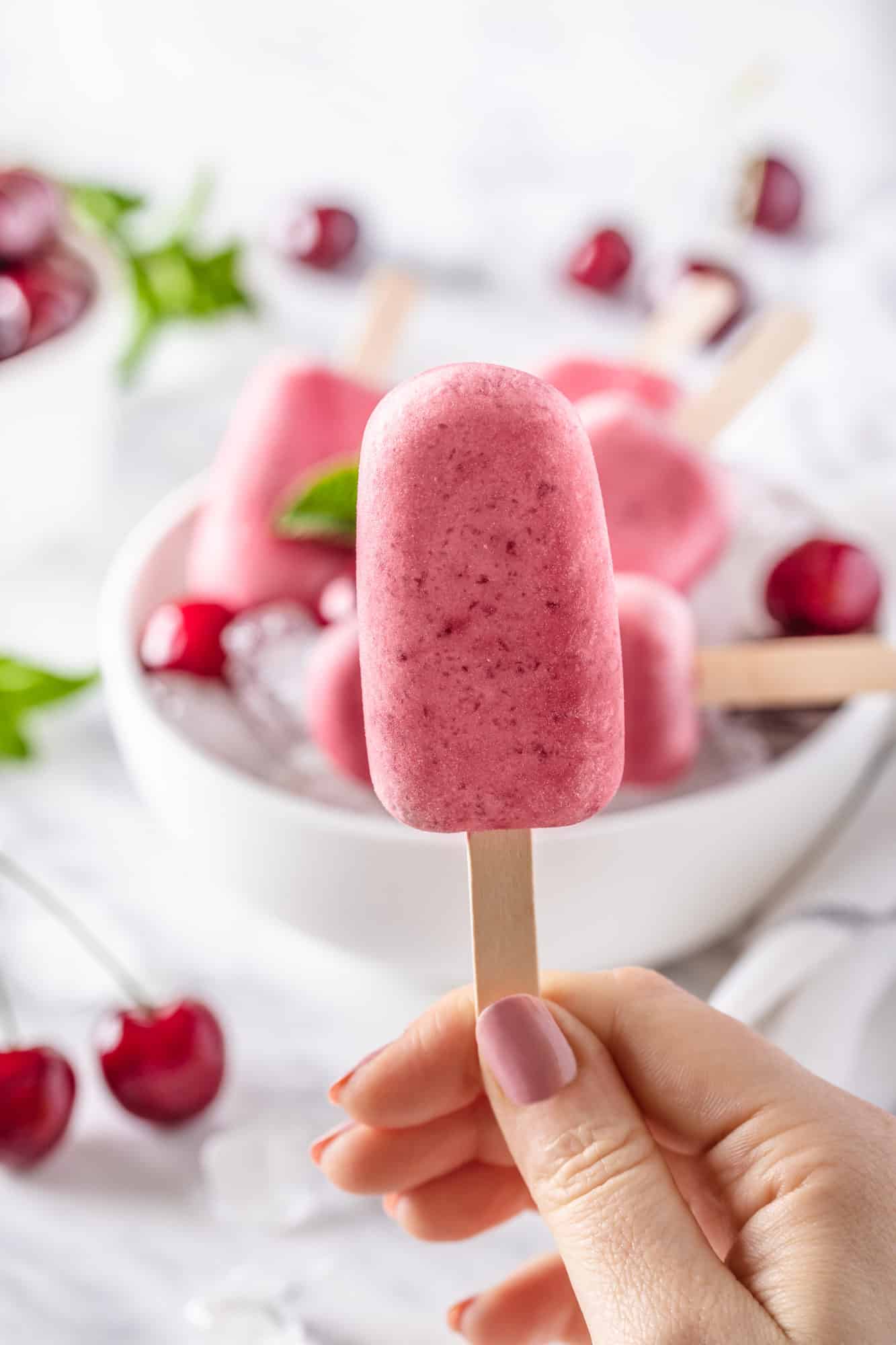 cherry ice pops on a wooden stick with a bowl of ice in the background.