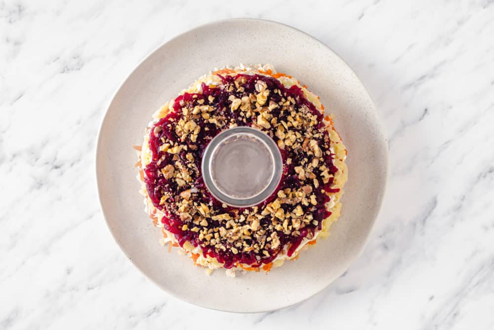 walnuts atop beets and other layers of a wreath salad on a white cream colored plate.