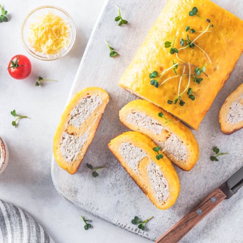 Sliced chicken and cheese roulade on a marble cutting board topped with a sprinkle of micro greens.