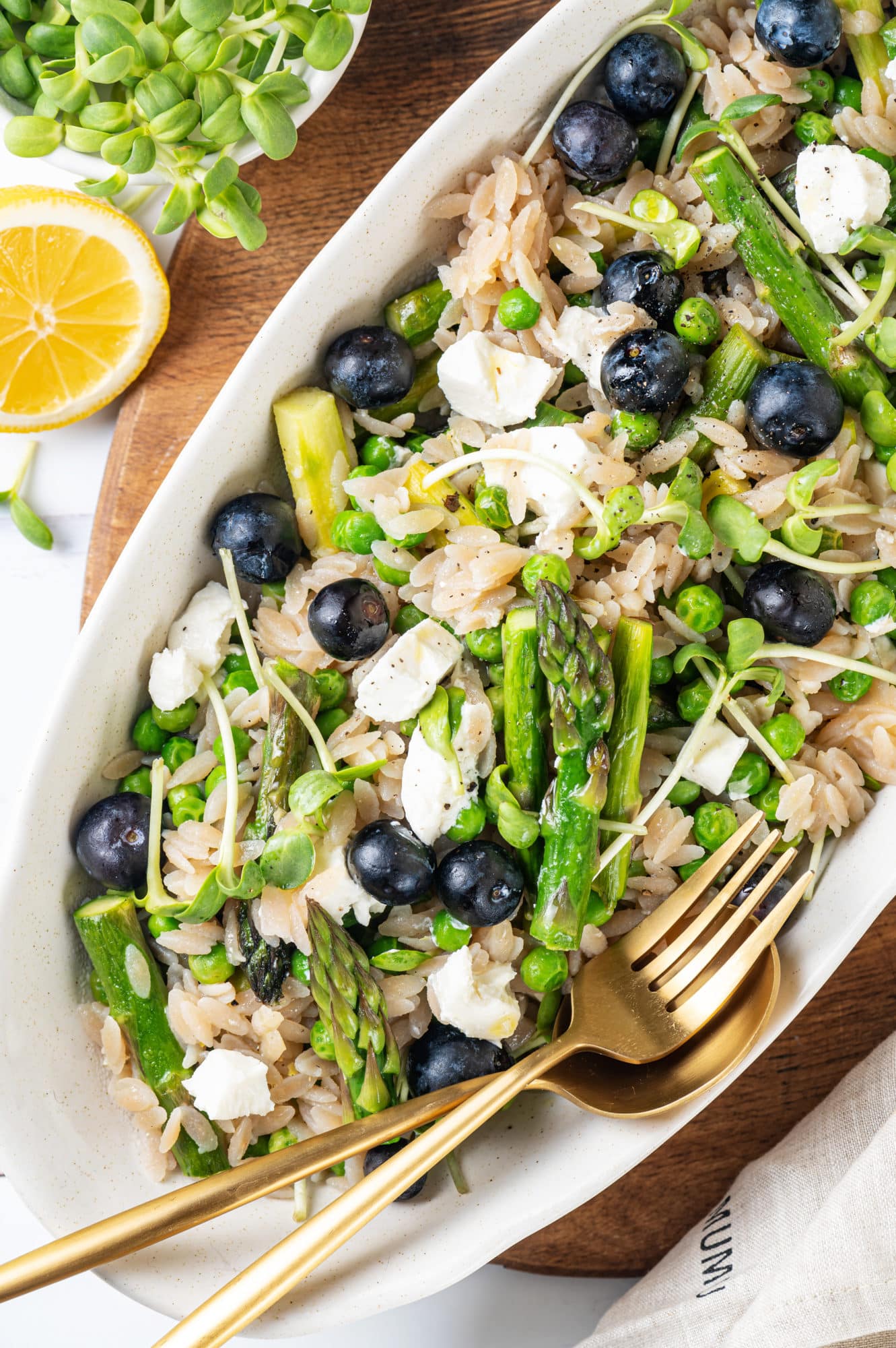 Orzo and lemon salad in a white oval shaped bowl with a fork and spoon in the bowl.