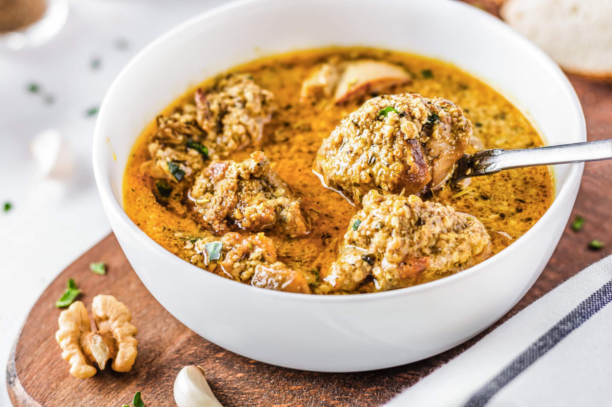 Georgian chicken in a white bowl on a wooden board with a spoon.