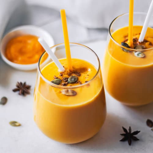 glasses with pumpkin smoothies in them and two straws.