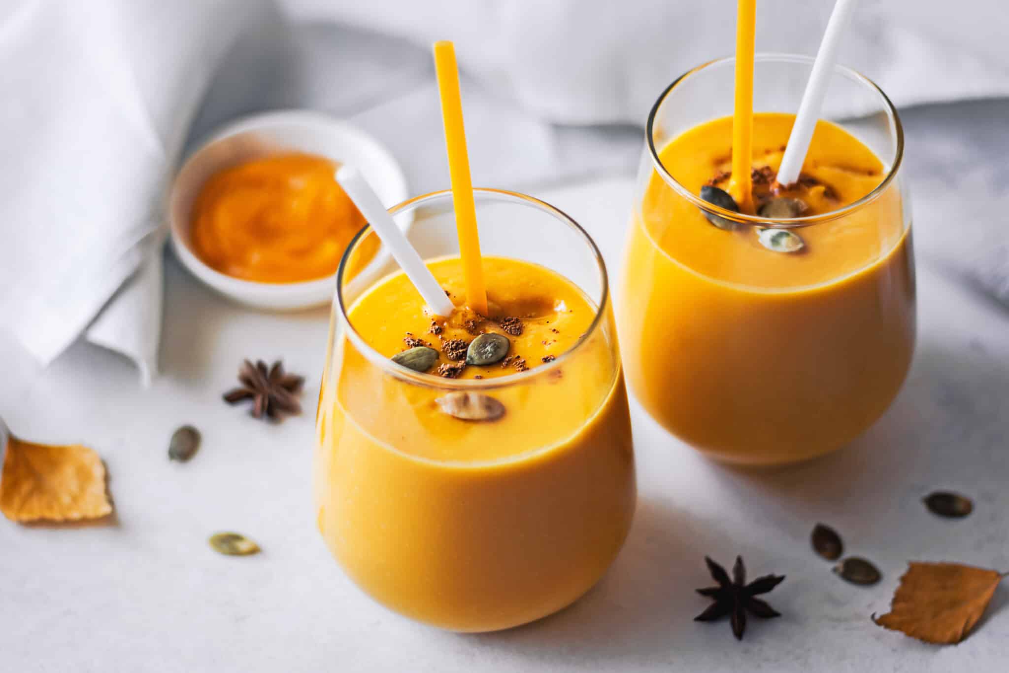 glasses with pumpkin smoothies in them and two straws.