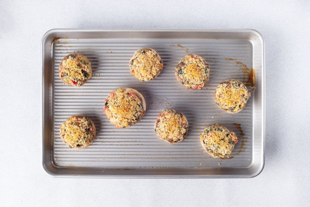 stuffed mushrooms baked on a grey baking tray.