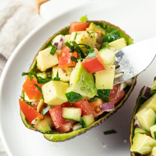 Avocado salad in avocado shells on a white plate with a fork.