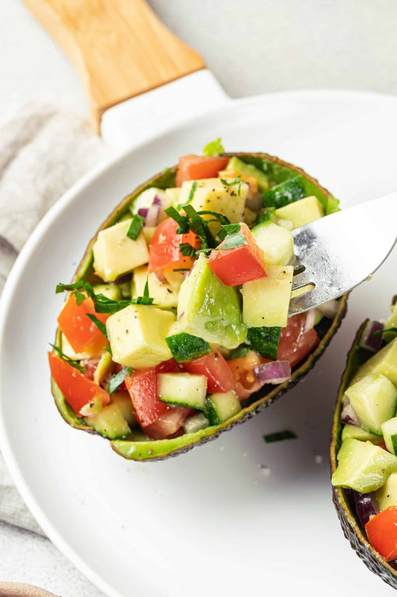 Avocado salad in avocado shells on a white plate with a fork.