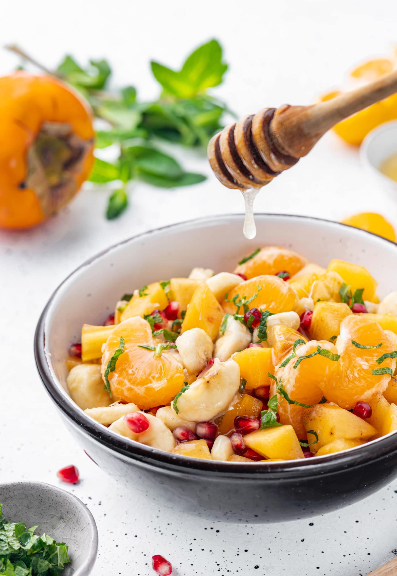 Persimmon fruit salad in a bowl with a honey dipper.