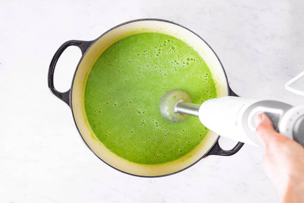 blended pea soup in a white and black pot with an immersion blender.