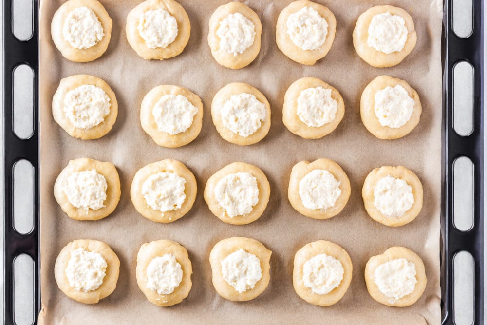 Raw Russian vatrushka buns with sweet cheese filling on a baking tray.