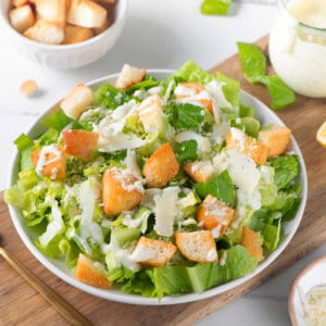 Caesar salad on a white plate with drizzled dressing, and croutons on top.