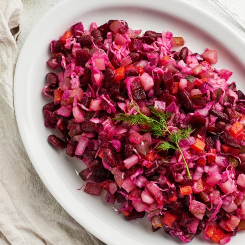 Vinegret salad on a large oval plate with dill on top and a spoon on the side.