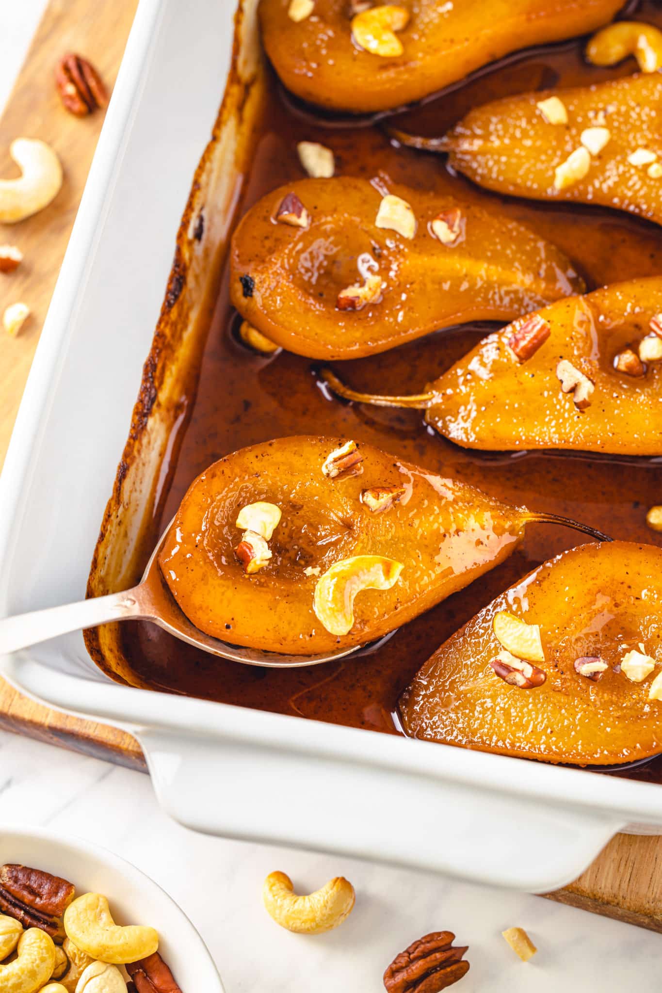 baked and roasted pears in a tray and on a spoon, covered in honey syrup and chopped walnuts