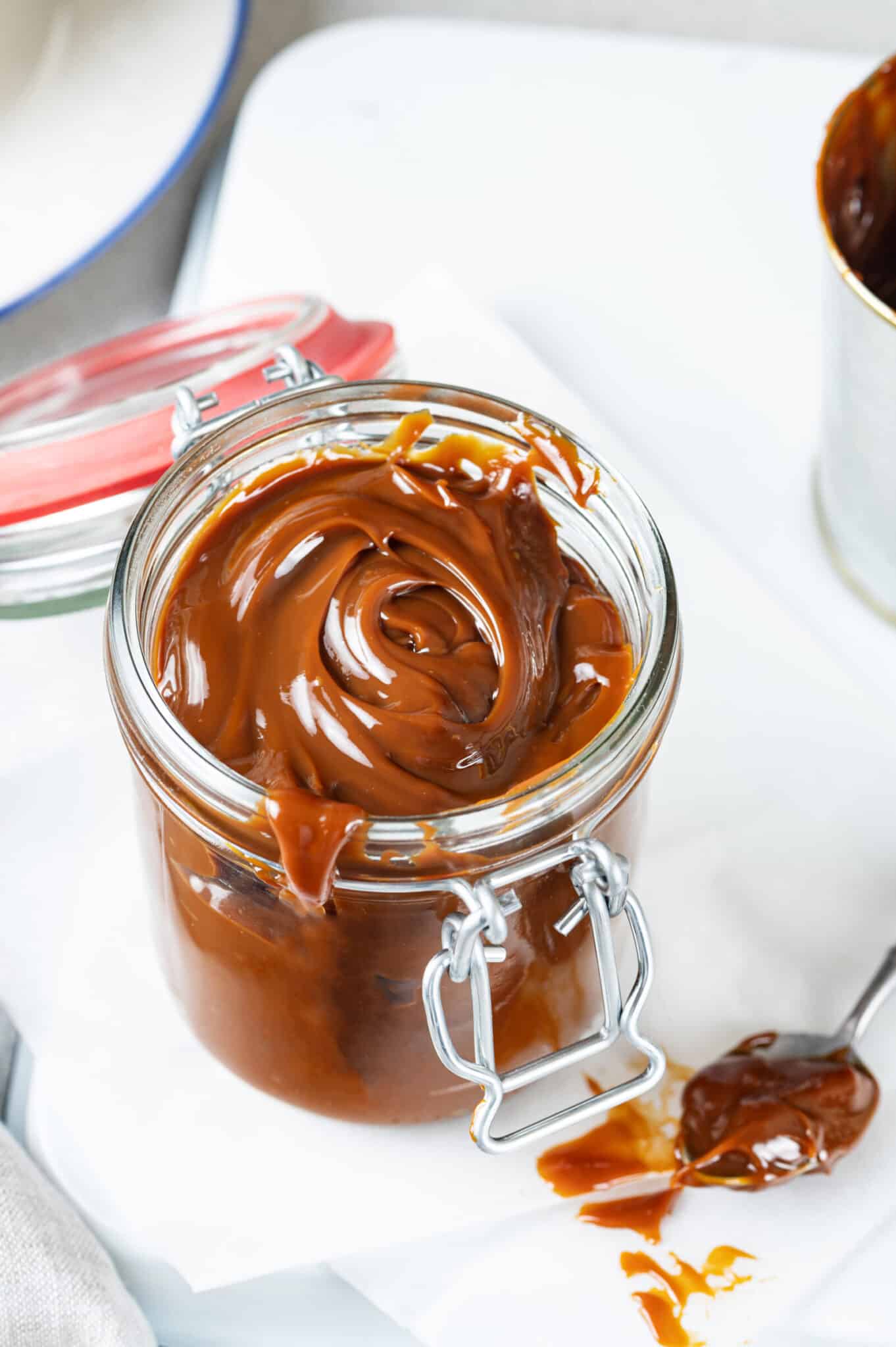 sweet dulce de leche in a glass jar with the lid open and a spoon of the leche on the table.