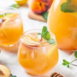 a glass of peach lemonade with more glasses of lemonade and a pitcher in the background.