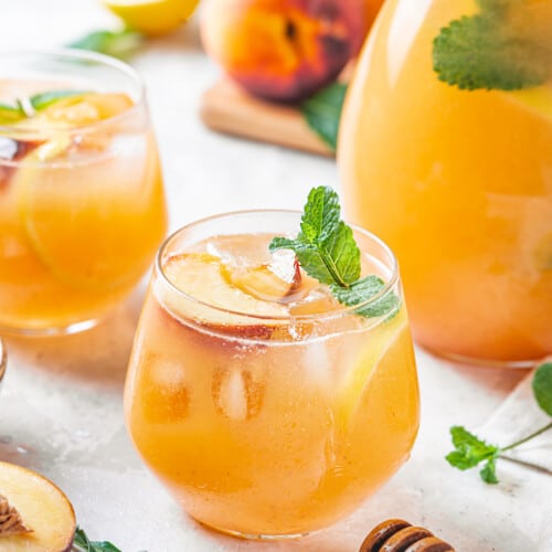 a glass of peach lemonade with more glasses of lemonade and a pitcher in the background.