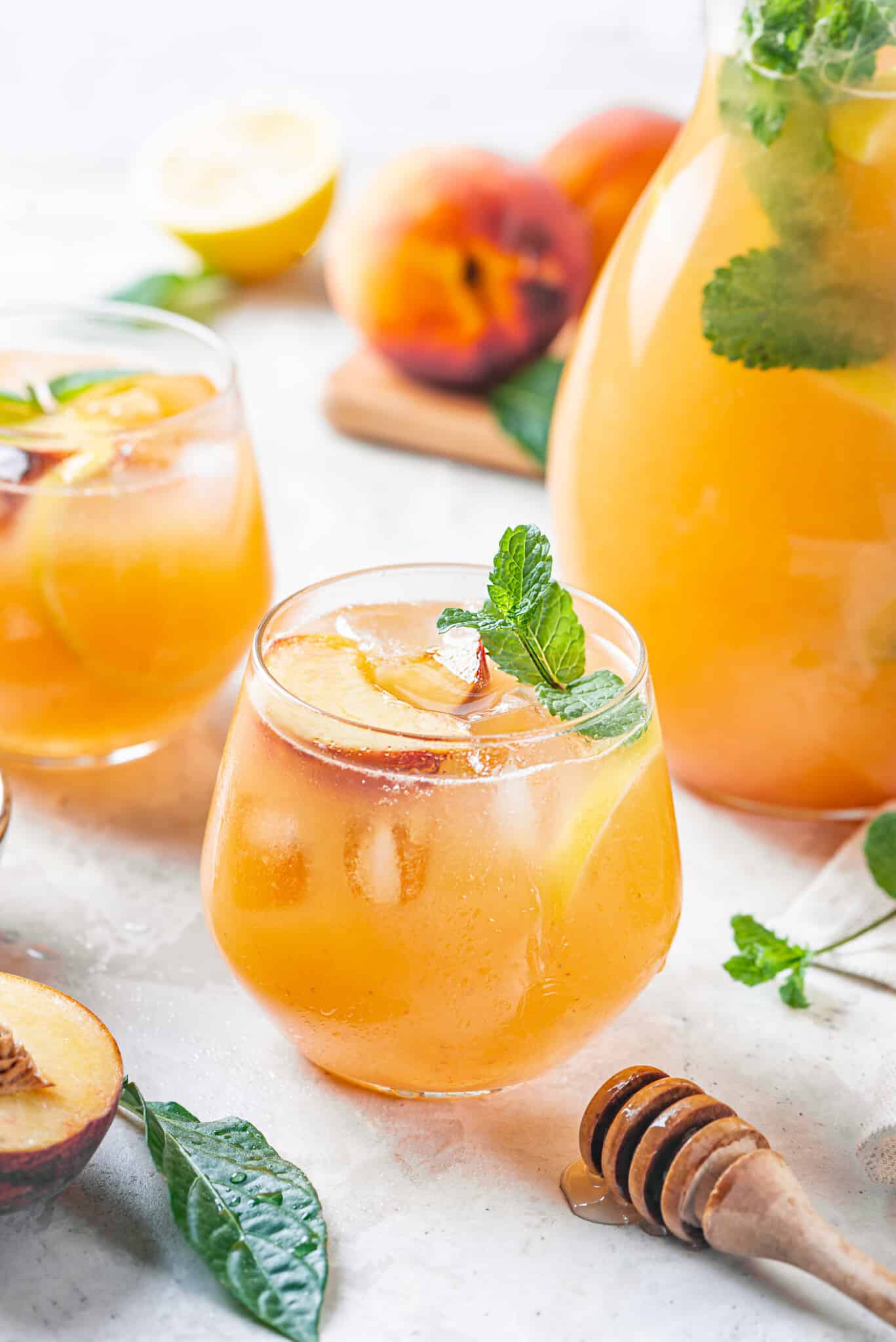 a glass of peach lemonade with more glasses of lemonade and a pitcher in the background.