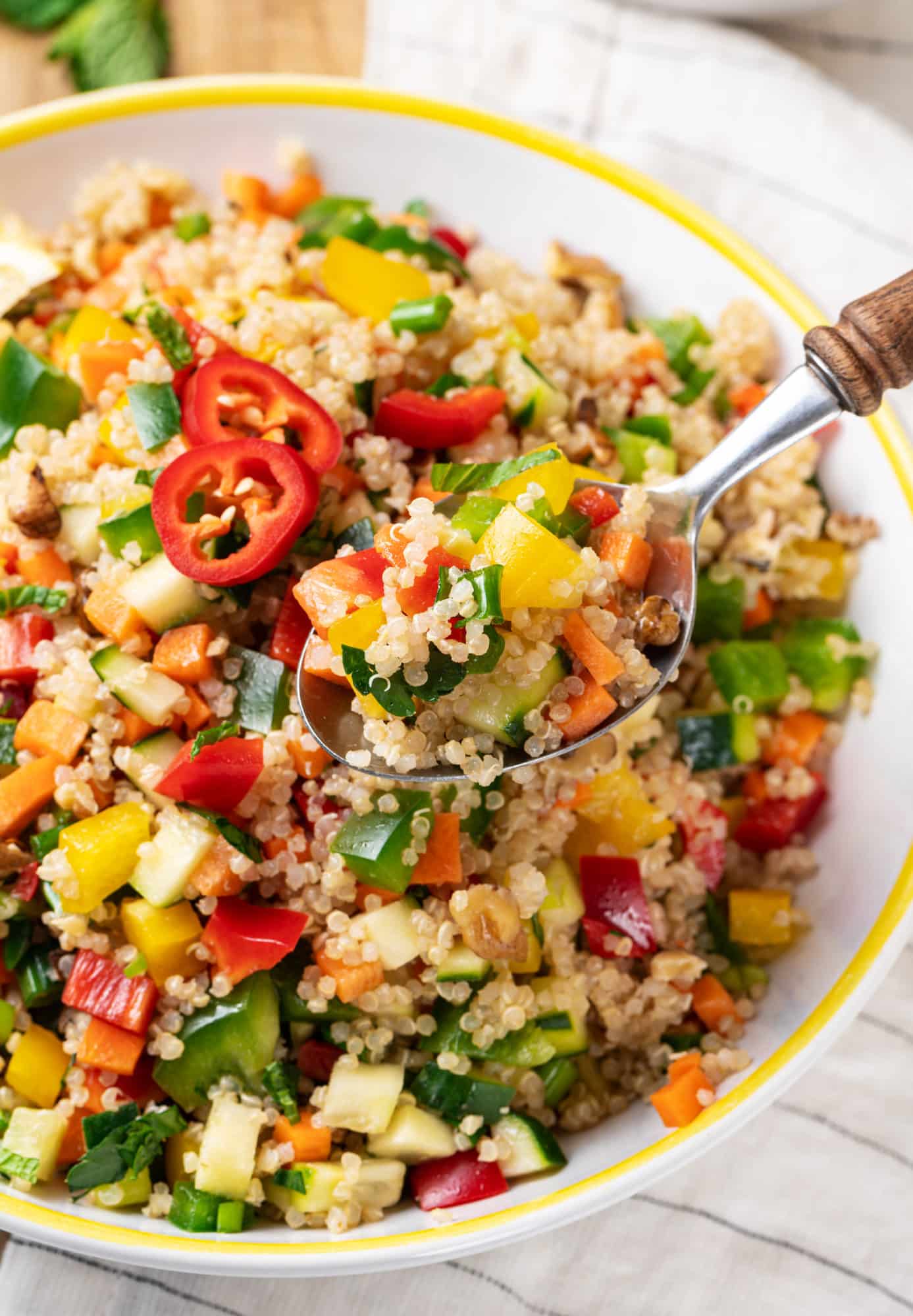 a spoon holding up quinoa salad and more salad in a bowl in the background.