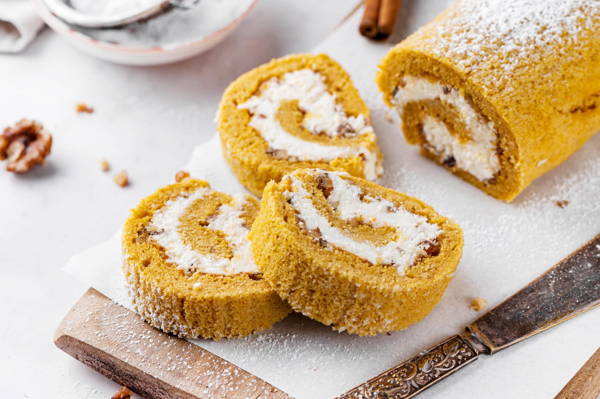 pumpkin-cake-roll-sliced-on-parchment-paper-and-a-wooden-board-with-a-knife