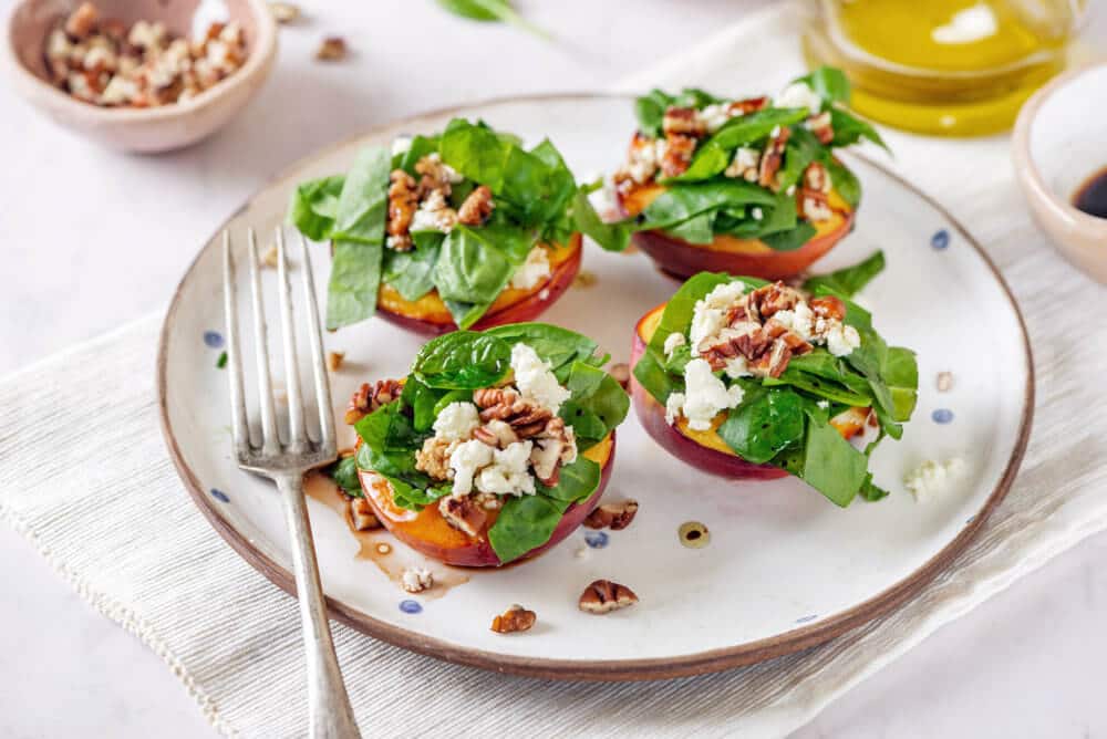 baked nectarine salad with greens nuts and cheese on top on a plate with a fork.